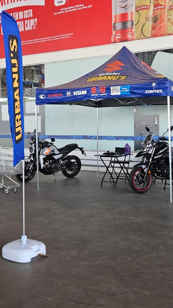 Tenda da Urbanu's com duas motos em exposição dentro do Mix Mateus, ao lado do banner Urbanu's
