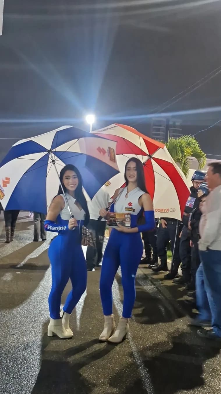 Duas promotoras da Urbanu's com sombrinhas no estande, à noite
